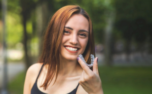 Woman outside, smiling, holding up her Invisalign